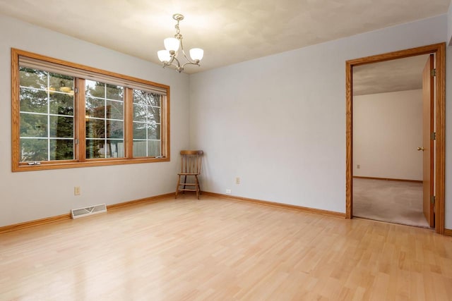 unfurnished room with light wood-style flooring, visible vents, a chandelier, and baseboards