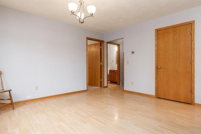 spare room featuring baseboards, light wood-style floors, and an inviting chandelier