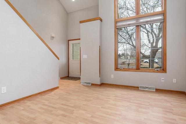 foyer entrance with light wood finished floors, a high ceiling, and visible vents