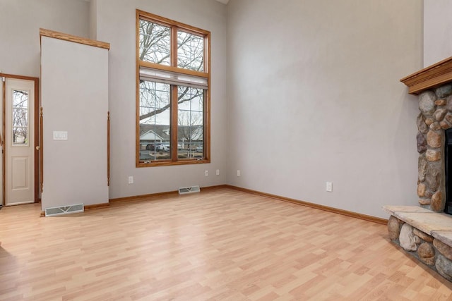 unfurnished living room featuring a towering ceiling, visible vents, and light wood-style floors