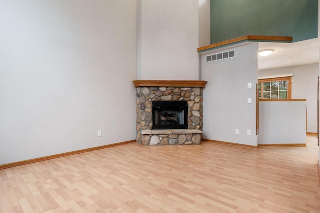 unfurnished living room with a stone fireplace, wood finished floors, visible vents, and baseboards