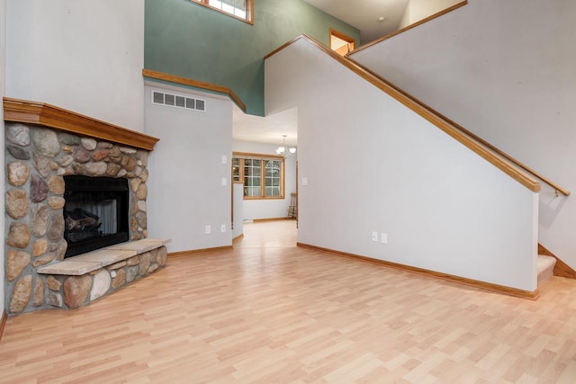 unfurnished living room with a stone fireplace, stairway, wood finished floors, and visible vents