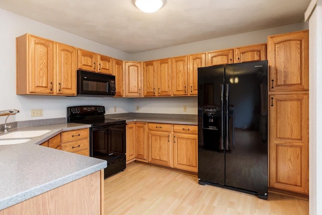 kitchen featuring black appliances, light wood-style floors, and a sink