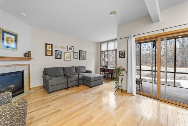 living area featuring a tiled fireplace, baseboards, and wood finished floors