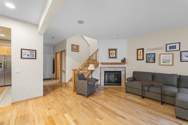 living room featuring light wood-type flooring, baseboards, a tiled fireplace, and stairs