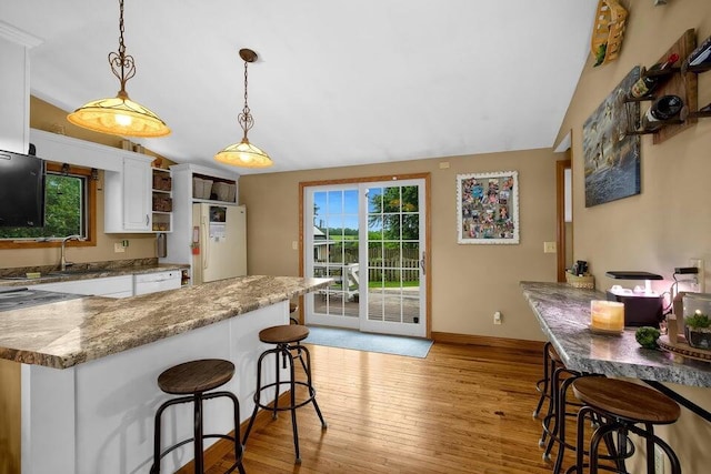 kitchen featuring light wood finished floors, a breakfast bar area, freestanding refrigerator, white cabinetry, and vaulted ceiling