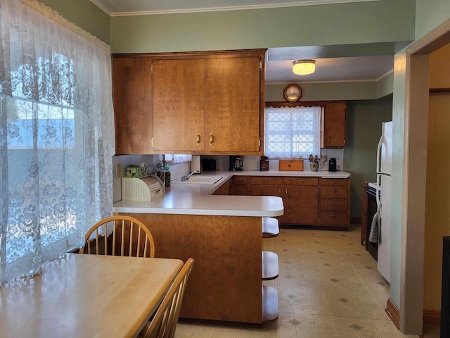 kitchen featuring a peninsula, crown molding, brown cabinetry, and light countertops