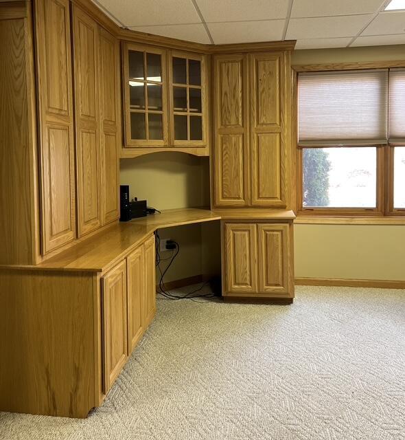 unfurnished office featuring baseboards, built in study area, a paneled ceiling, and light colored carpet