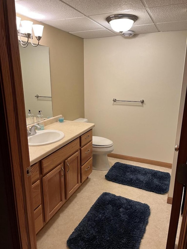 bathroom featuring toilet, baseboards, a drop ceiling, and vanity