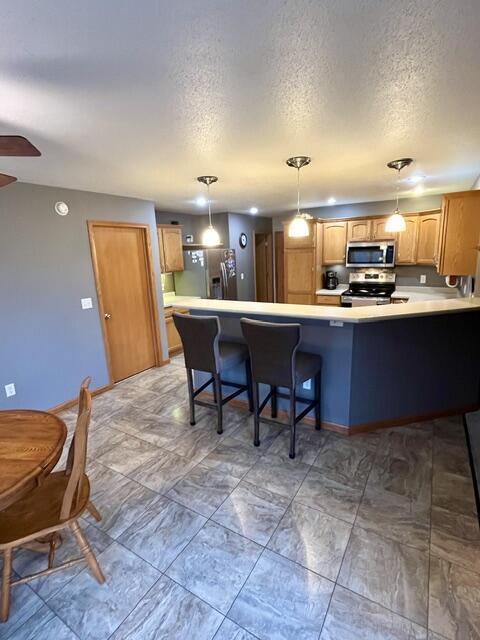 kitchen featuring a peninsula, appliances with stainless steel finishes, light countertops, and pendant lighting