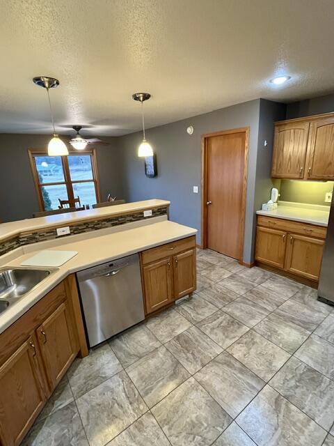 kitchen featuring brown cabinets, pendant lighting, stainless steel dishwasher, and light countertops