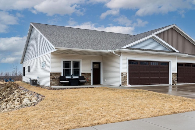 view of front of property featuring an attached garage, stone siding, central AC unit, and roof with shingles