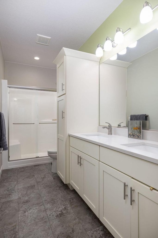 full bathroom featuring double vanity, a shower stall, toilet, and a sink