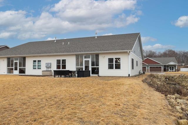 back of property with a garage, roof with shingles, and a lawn