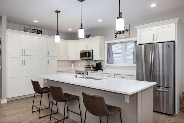 kitchen featuring a breakfast bar, appliances with stainless steel finishes, light wood-style floors, white cabinetry, and a sink