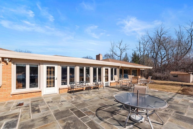 rear view of property featuring brick siding, a chimney, outdoor dining area, a patio area, and an outbuilding