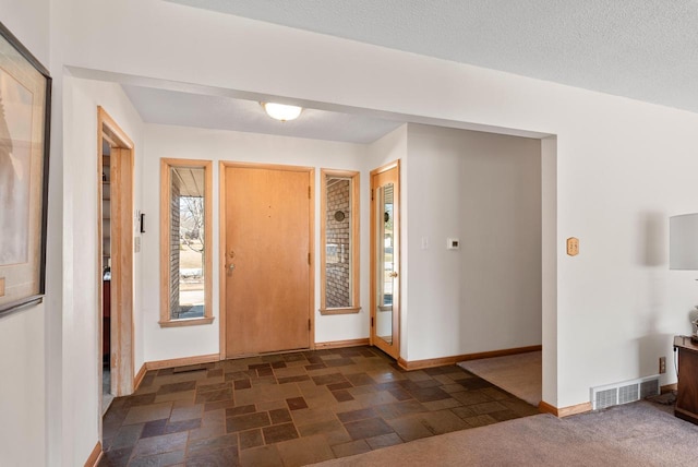 entrance foyer featuring stone finish flooring, baseboards, visible vents, and a textured ceiling