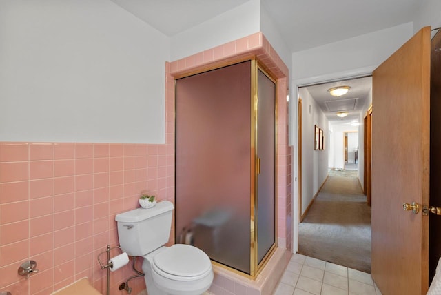 bathroom featuring tile patterned floors, toilet, tile walls, wainscoting, and a shower stall