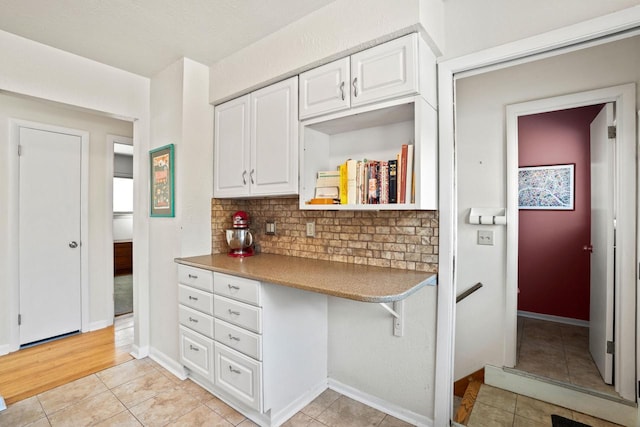 kitchen with tasteful backsplash, white cabinetry, light tile patterned flooring, baseboards, and built in study area