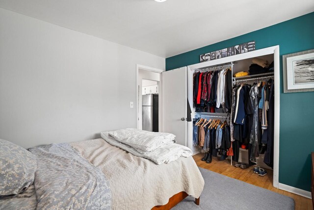 bedroom featuring a closet, freestanding refrigerator, and wood finished floors