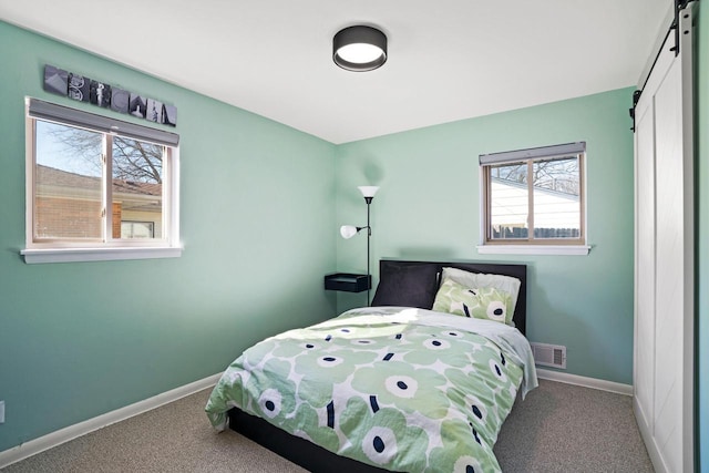 bedroom with a barn door, visible vents, baseboards, and carpet floors