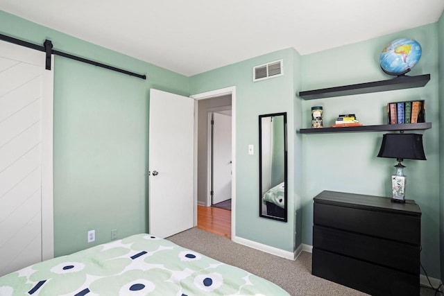 bedroom featuring a barn door, carpet, visible vents, and baseboards