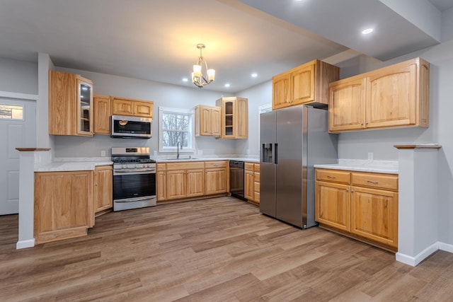 kitchen featuring appliances with stainless steel finishes, glass insert cabinets, a sink, and light wood-style flooring