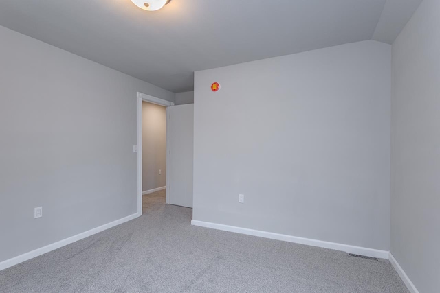 carpeted spare room featuring lofted ceiling, visible vents, and baseboards