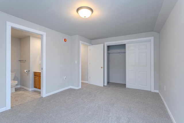 unfurnished bedroom with baseboards, a closet, ensuite bath, and light colored carpet