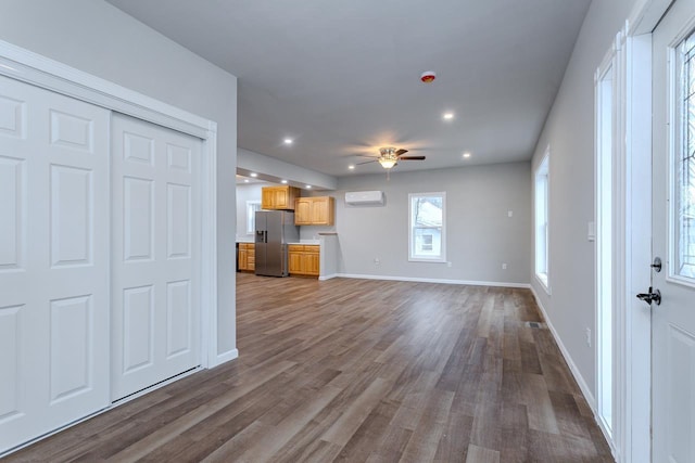 unfurnished living room featuring dark wood-style flooring, a wall unit AC, a ceiling fan, and baseboards