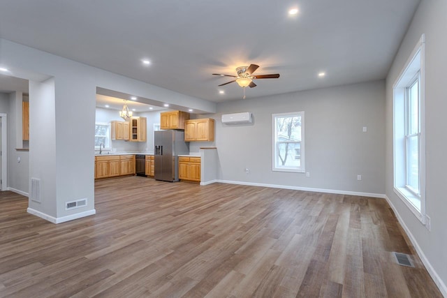 unfurnished living room with recessed lighting, light wood-style flooring, a wall mounted air conditioner, baseboards, and ceiling fan with notable chandelier