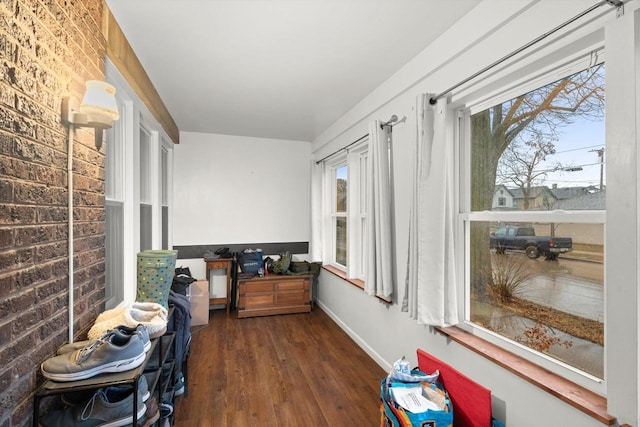 interior space with a wealth of natural light, baseboards, brick wall, and wood finished floors