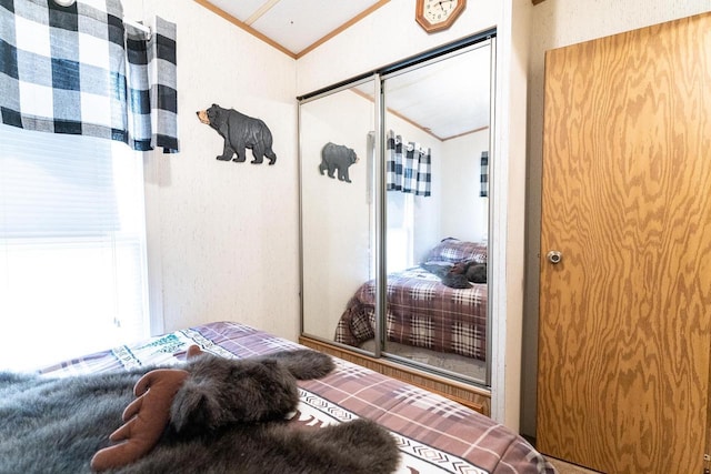 bedroom featuring lofted ceiling, ornamental molding, and a textured wall