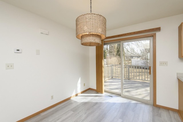 unfurnished dining area featuring a notable chandelier, baseboards, and light wood finished floors