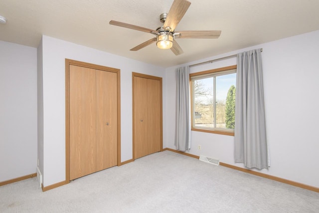 unfurnished bedroom with visible vents, baseboards, multiple closets, light carpet, and a ceiling fan