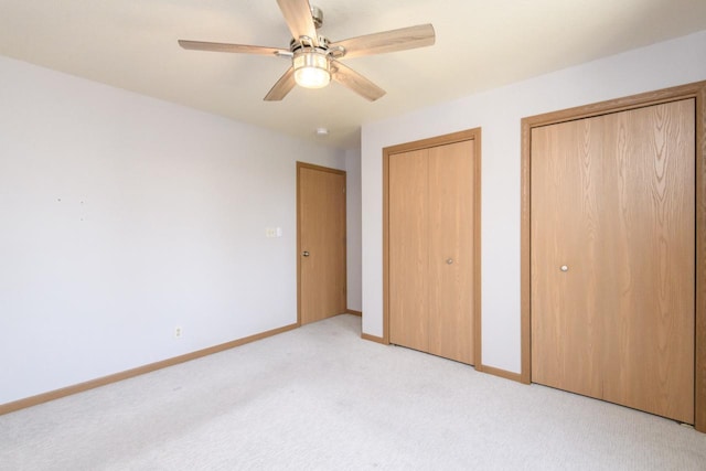 unfurnished bedroom with ceiling fan, baseboards, multiple closets, and light carpet