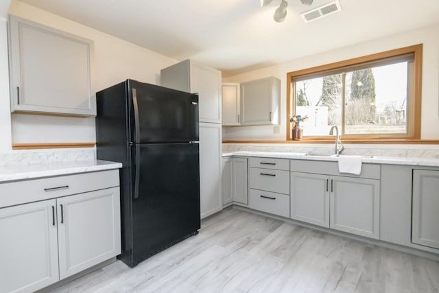 kitchen with visible vents, gray cabinets, freestanding refrigerator, and a sink