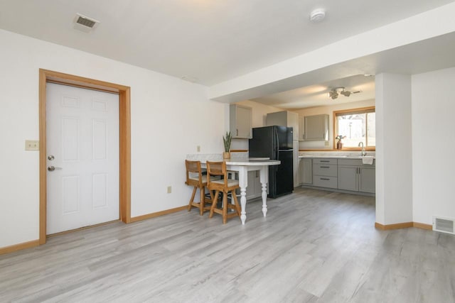 kitchen featuring visible vents, baseboards, light wood-type flooring, gray cabinets, and freestanding refrigerator