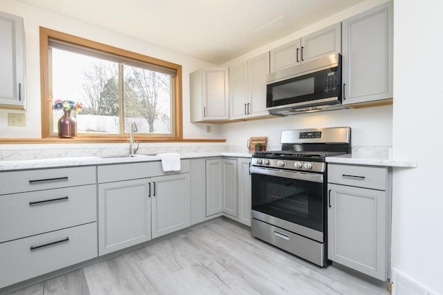 kitchen with stainless steel gas range oven, visible vents, gray cabinetry, and a sink