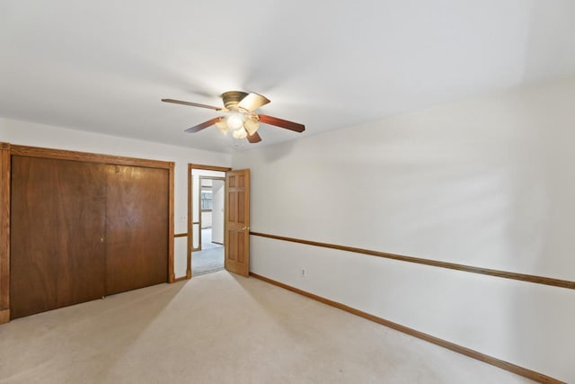 unfurnished bedroom with a closet, light colored carpet, a ceiling fan, and baseboards