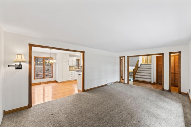 unfurnished living room with visible vents, light colored carpet, a chandelier, and stairs