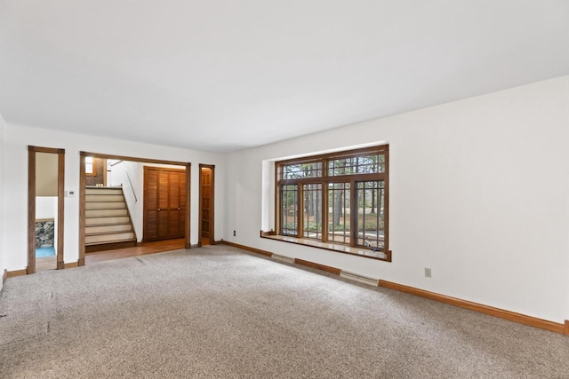 carpeted spare room with stairway, visible vents, and baseboards