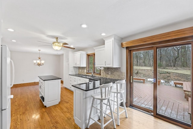 kitchen with dark countertops, tasteful backsplash, freestanding refrigerator, white cabinetry, and a sink