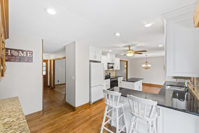 kitchen with light wood finished floors, decorative backsplash, appliances with stainless steel finishes, a peninsula, and white cabinetry