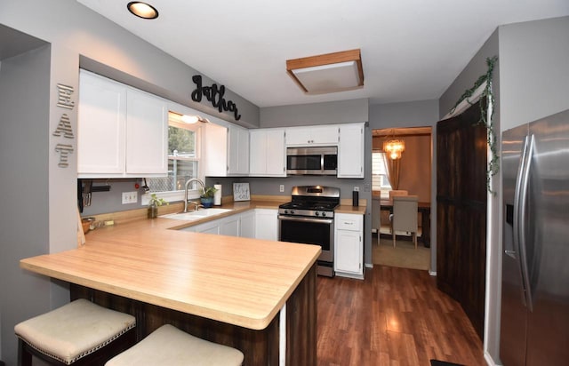 kitchen with stainless steel appliances, light countertops, white cabinets, a sink, and a peninsula