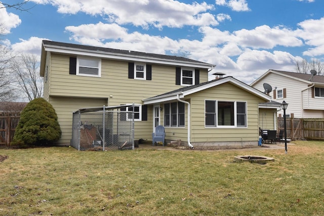 rear view of property with an outdoor fire pit, a lawn, and fence