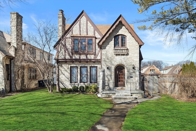 tudor-style house with stone siding, fence, and a front yard