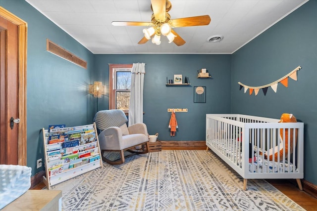 bedroom with a nursery area, baseboards, visible vents, and wood finished floors