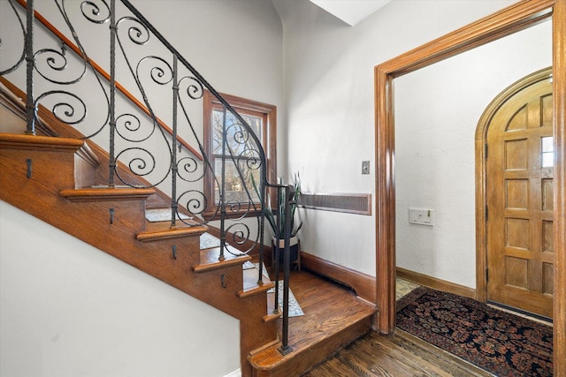 entrance foyer featuring arched walkways, stairway, baseboards, and wood finished floors