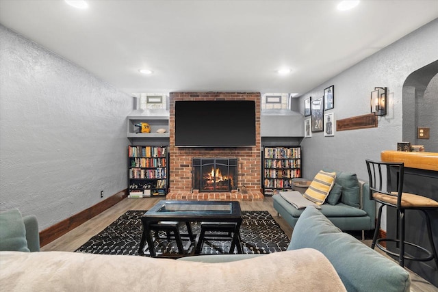 living room featuring a textured wall, a brick fireplace, wood finished floors, and baseboards